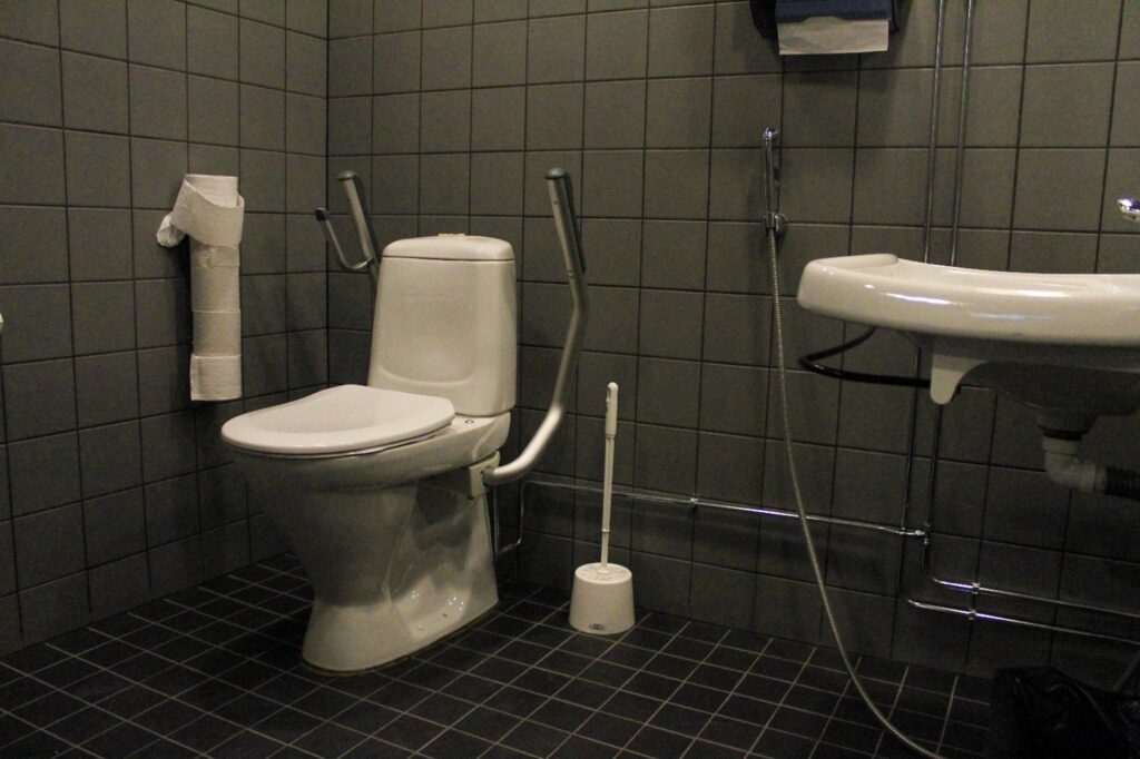 WC-pönttö. jossa on ylös nostettavat kahvat. WC-paperiteline on istuessa oikealla puolella.