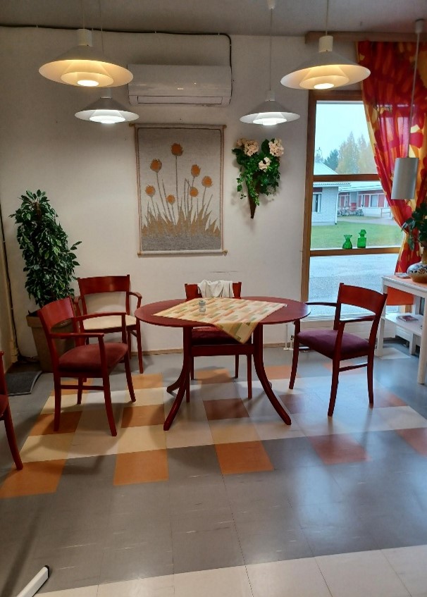 Palvelutalon sisätilaa, tummanpunainen pöytäryhmä. Pöydällä virkattu pöytäliina.