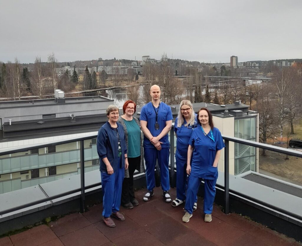 Projektiryhmä seisoo katolla, melkein kaikilla heistä on hoitajan vaatteet päällä.