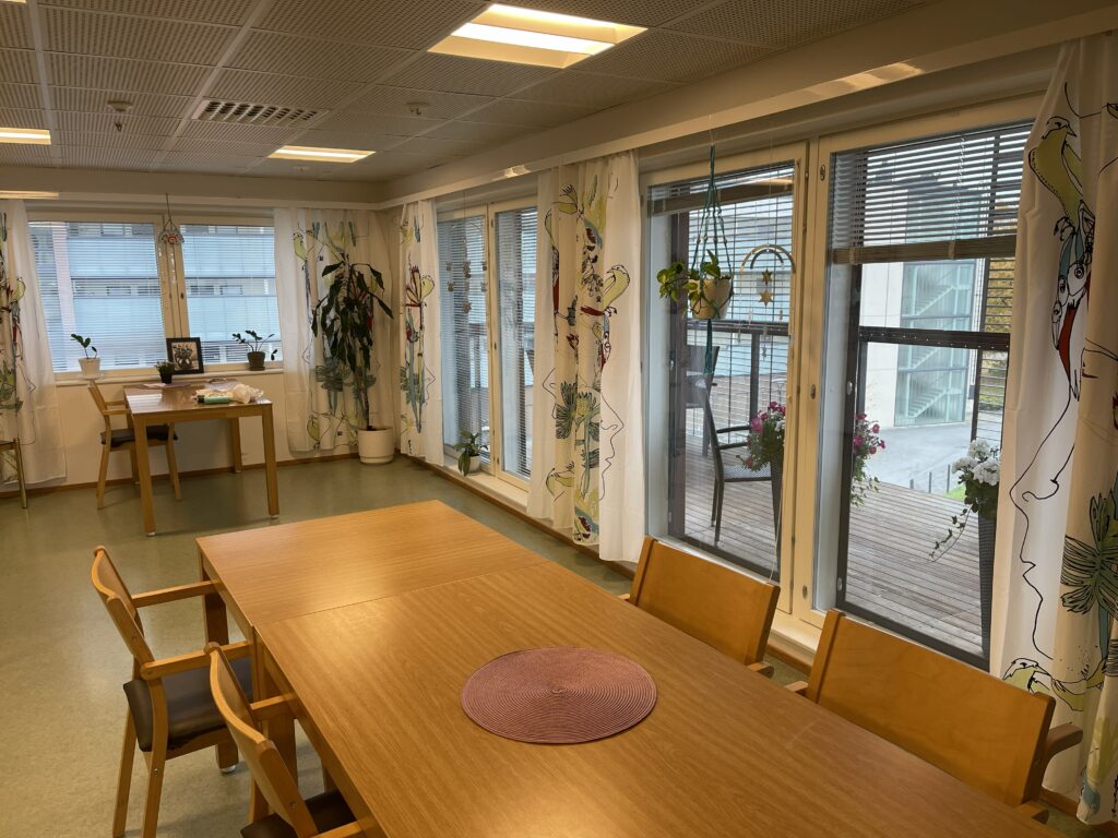 Matti-talo sisältä. Pitkä pöytä, isot ikkunat, joissa verhot ja näkymä parvekkeelle.