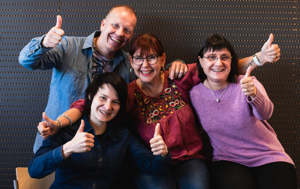 Ryhmä Ikäinstituutin työntekijöitä näyttää peukkuja kameralle ja hymyilee.